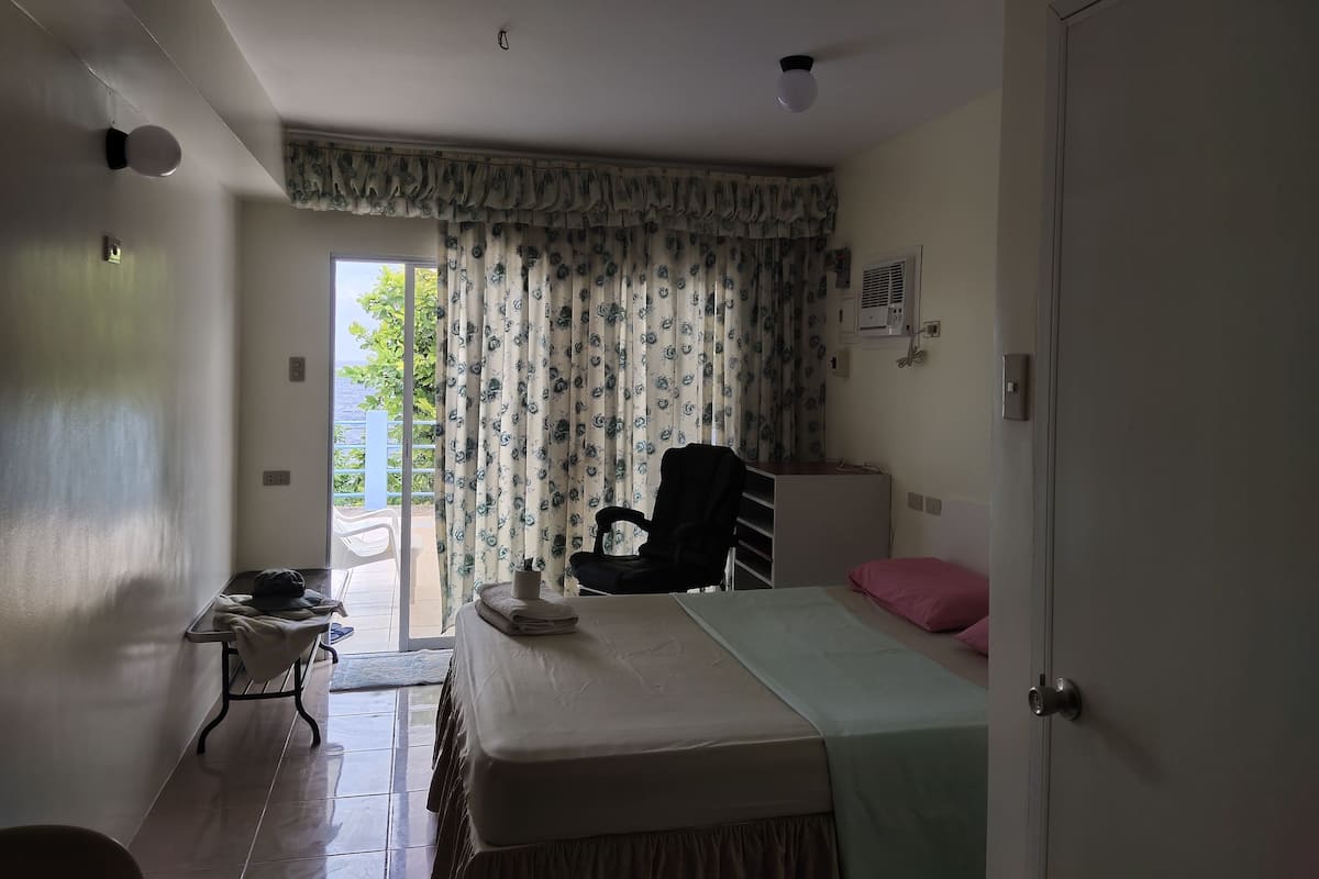 A bedroom with a bed, a chair, a desk, and a window with curtains.
