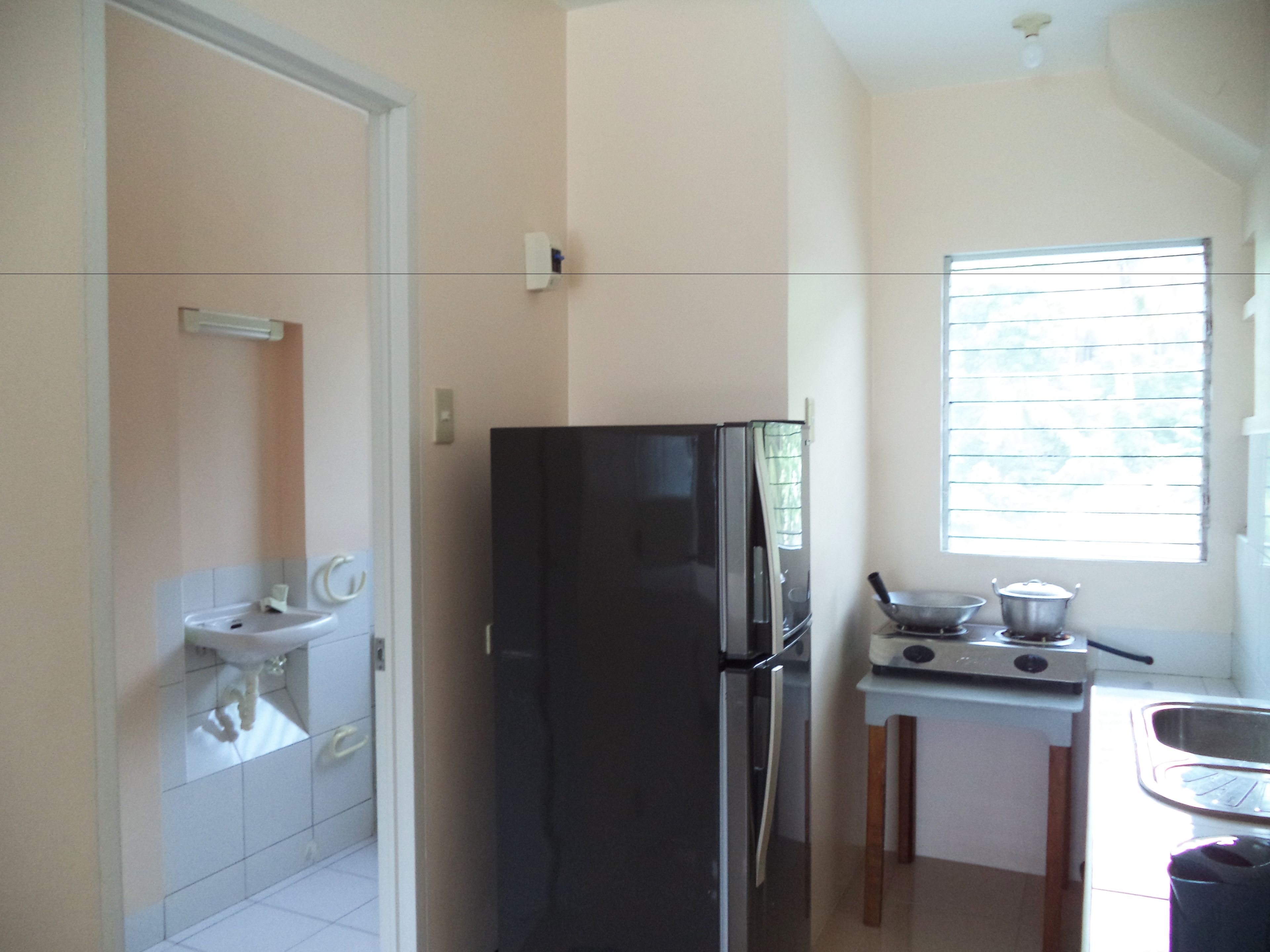 A compact kitchen with a refrigerator, stove, and a window with blinds.