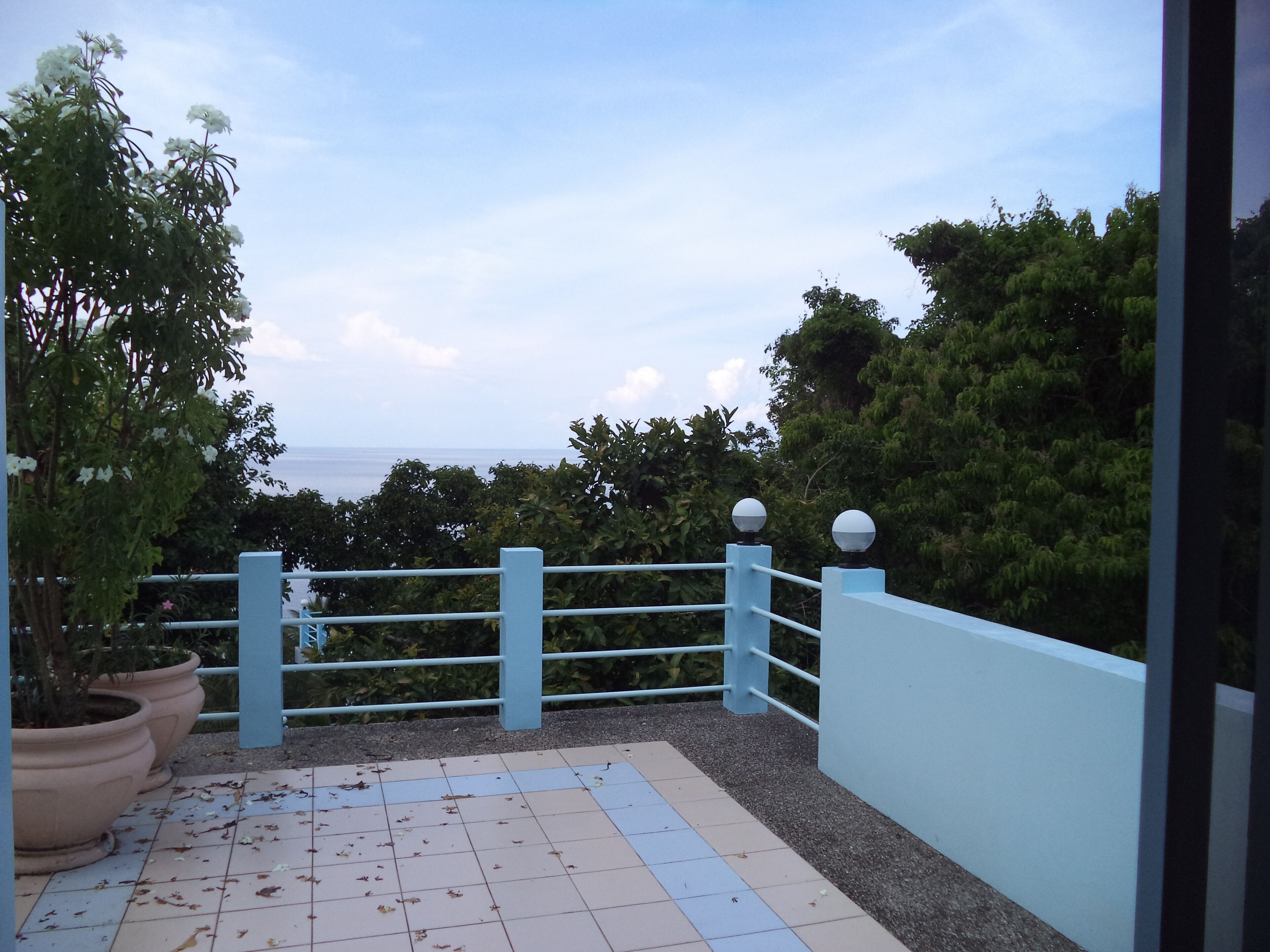 A balcony with a tiled floor, potted plants, and a railing with spherical lights.