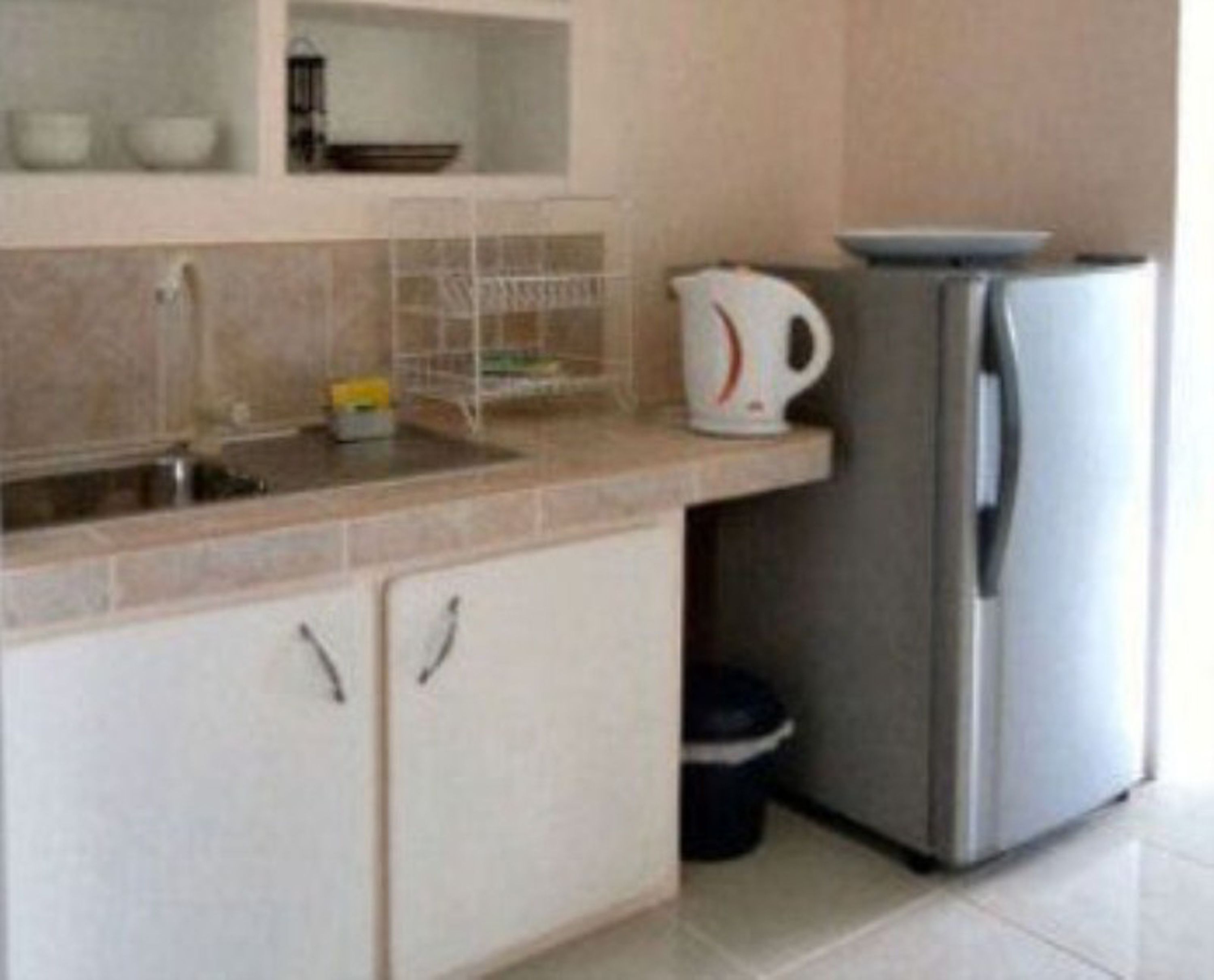 A kitchen with a sink, a kettle, a refrigerator, and a trash bin.