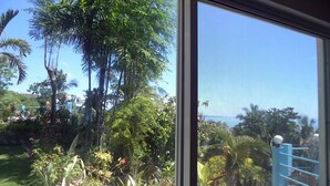 A view of a lush garden with various plants and trees, visible through a window with a metal grill. - High Steps Pension (Catmon)
