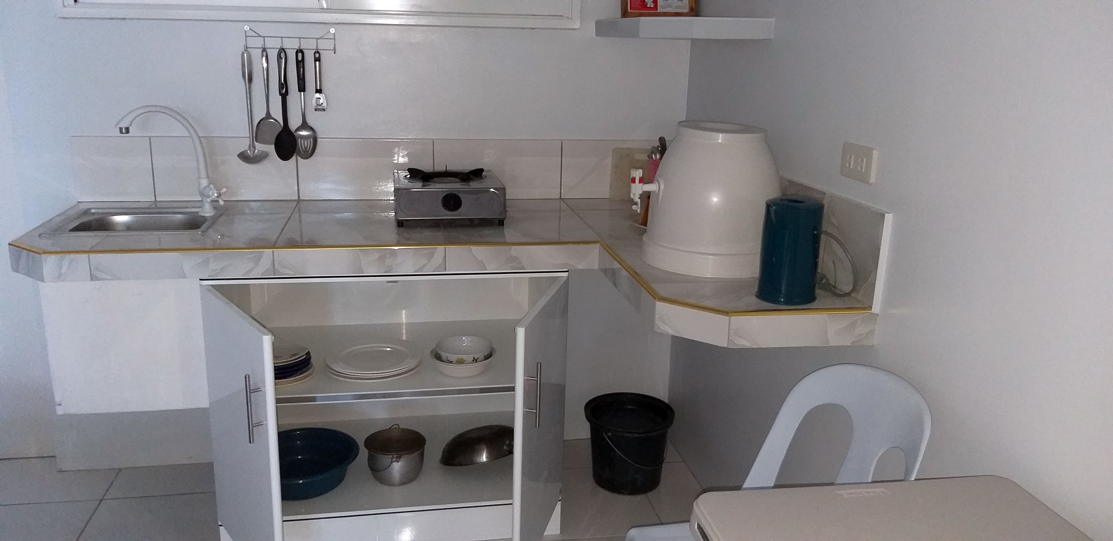 A compact kitchen with a sink, stove, and shelves for dishes and utensils.