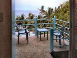 A view from a balcony with a metal railing, overlooking a beach with palm trees and the ocean.
