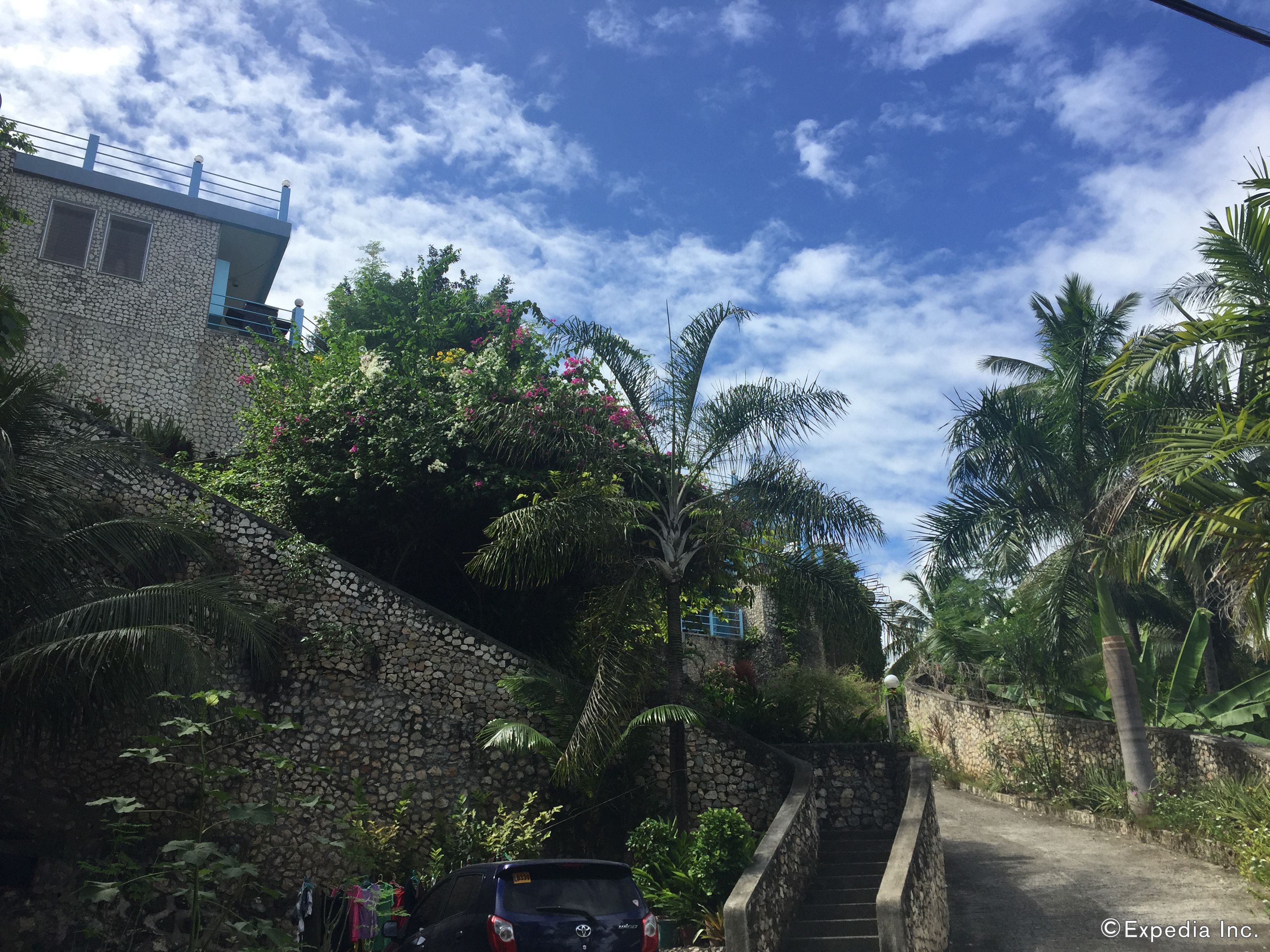 A narrow street with a stone wall on one side and a building with a balcony on the other.