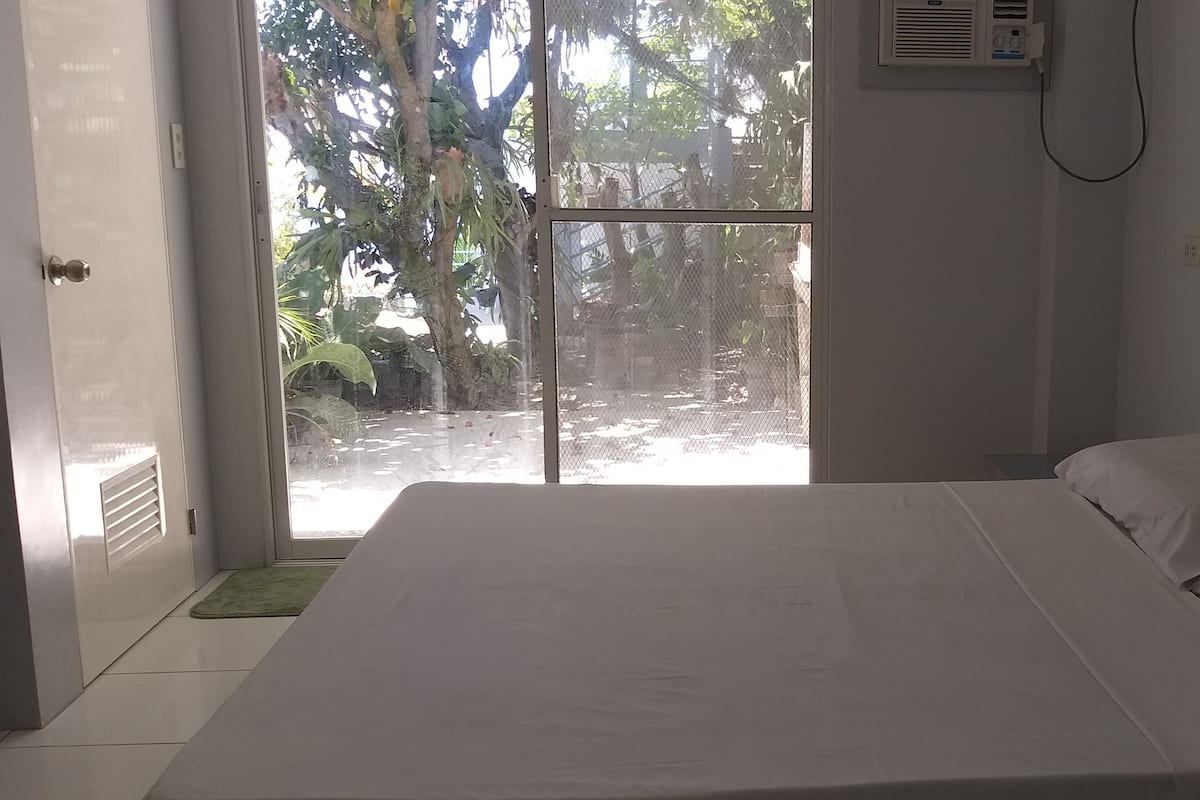 A bedroom with a bed, a door leading to a balcony, and a wall-mounted air conditioning unit.