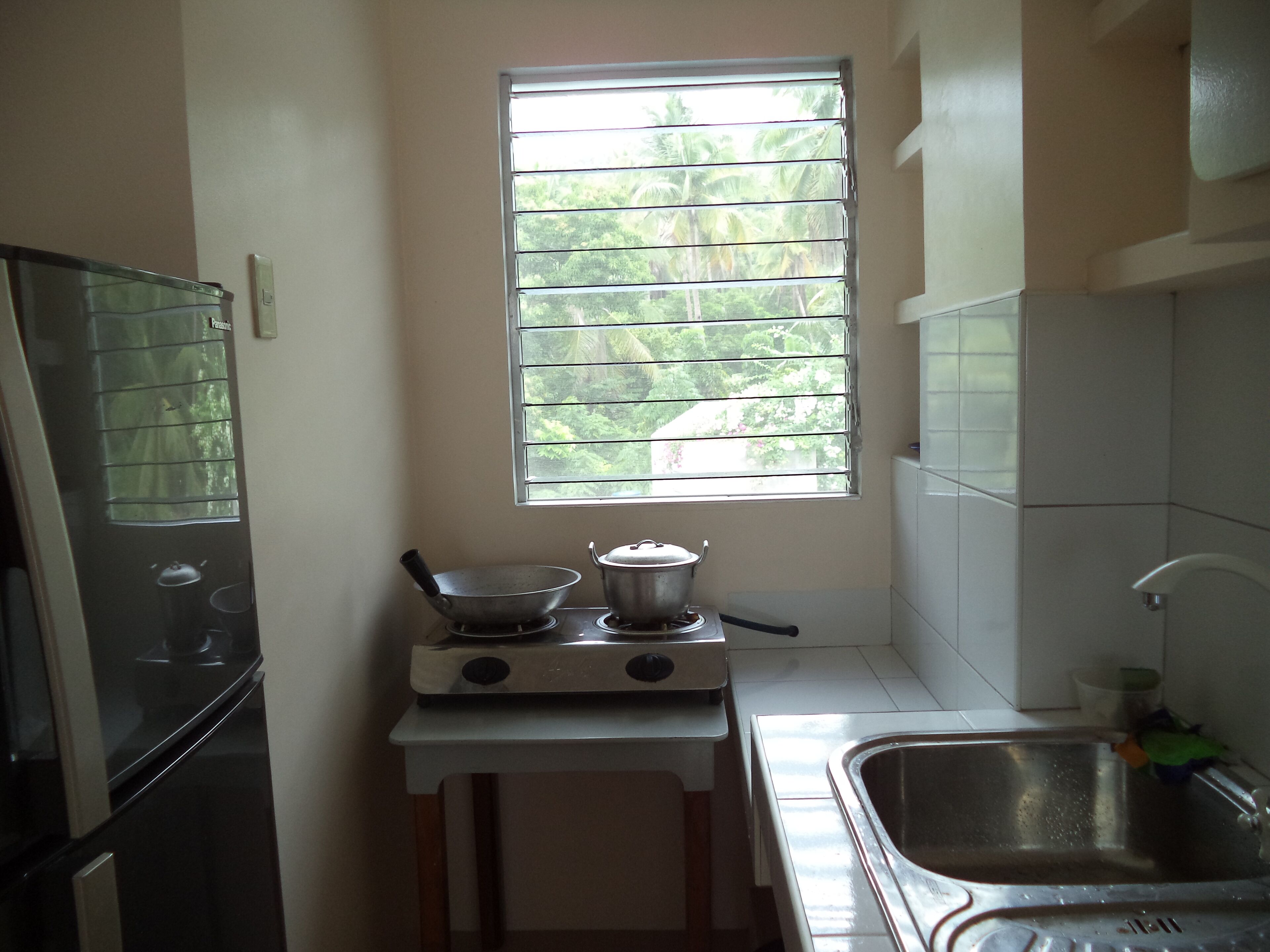 Una cocina compacta con ventana, estufa, lavamanos y refrigerador.