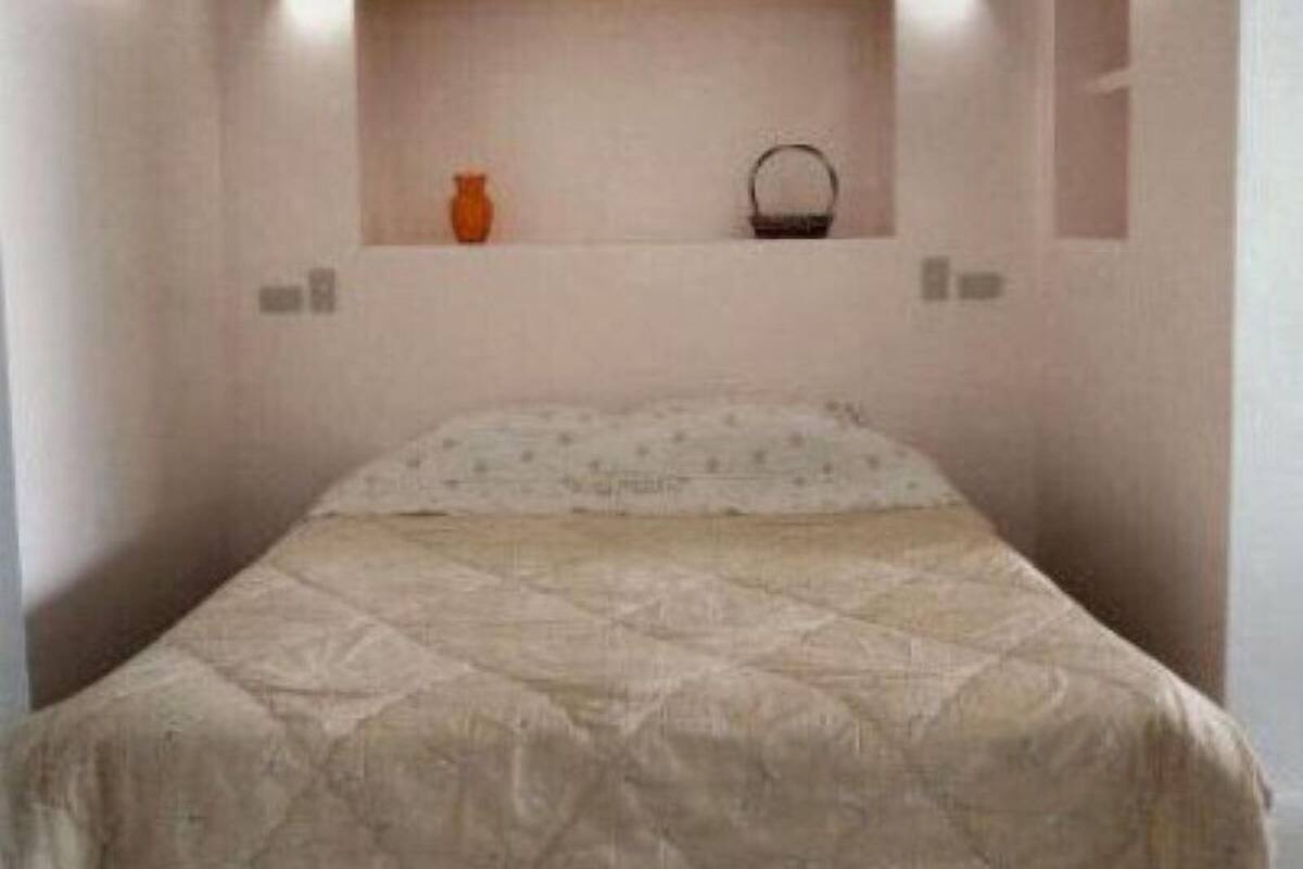 A bedroom with a bed, a wall-mounted shelf with a vase and a basket, and a small mirror.