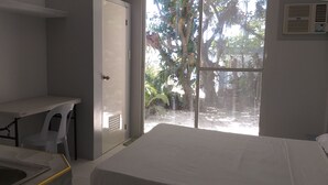 A hotel room with a bed, a desk, and a window overlooking a garden. - High Steps Pension (Catmon)