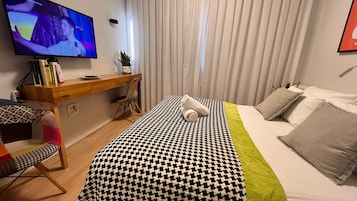 A hotel room with a bed, a desk, a chair, a TV, and curtains.