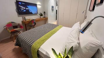 A hotel room with a bed, a desk, a chair, a TV, and a wardrobe.