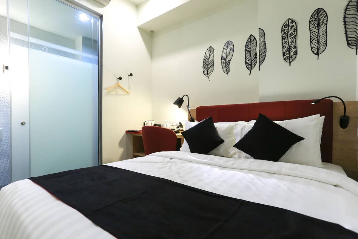 A hotel room with a bed, a desk, a chair, and a wall with feather decorations.