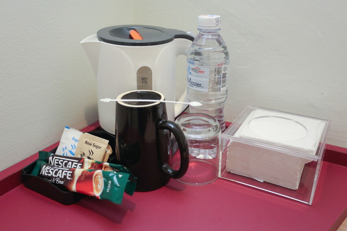 Una bandeja con cafetera, botella de agua, taza, paquete de Nescafé y un pastel en una caja transparente.
