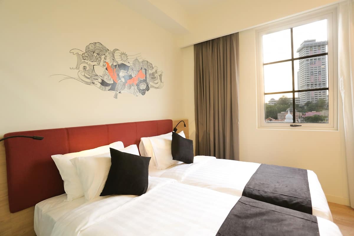 A hotel room with a large bed, a red headboard, a window with curtains, and a wall mural.