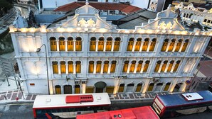 Un edificio blanco con varias ventanas y un autobús rojo estacionado adelante.