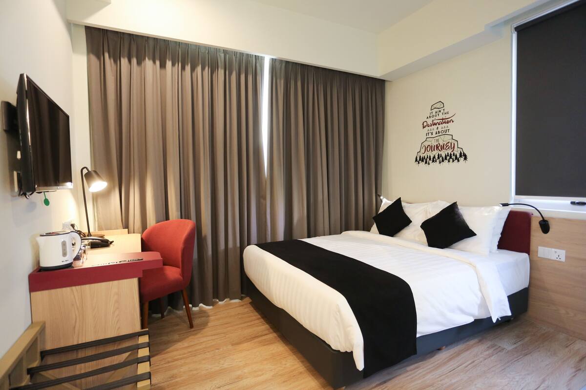 A hotel room with a bed, a desk with a lamp, a chair, and a television.