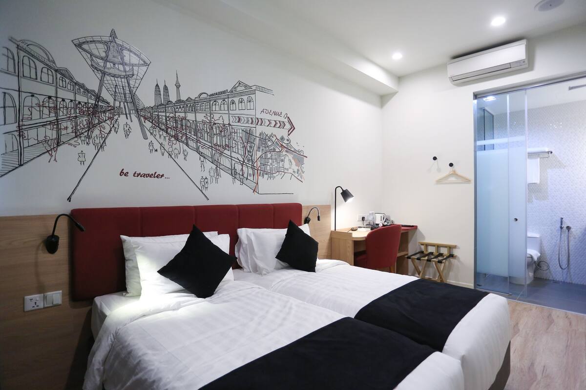 A hotel room with a large bed, a red headboard, a wall map, a desk, and a shower area.