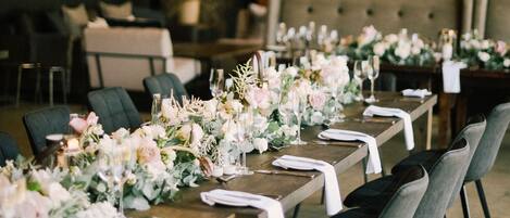 Una larga mesa de comedor con sillas, una araña y centros de mesa florales.