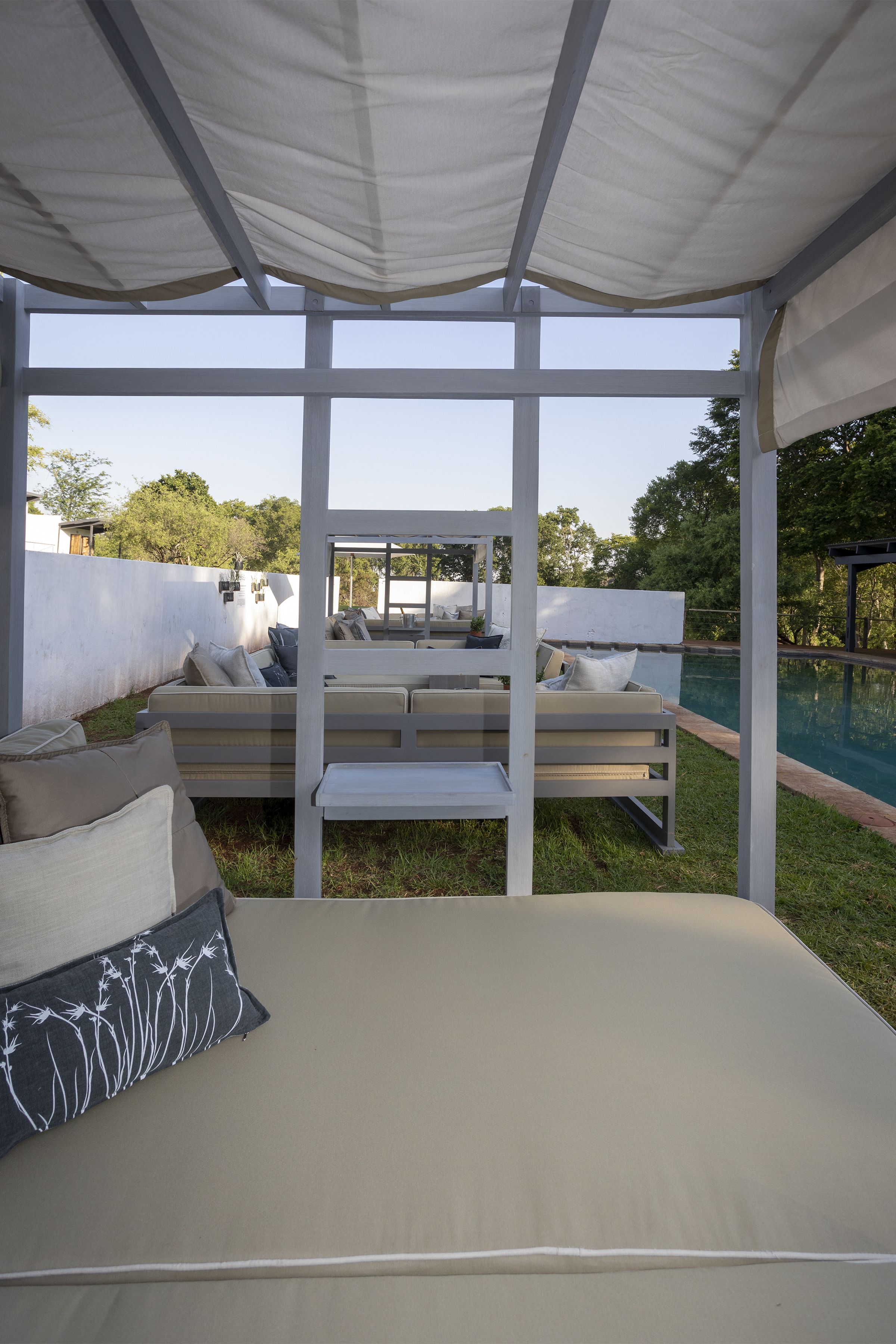 A covered outdoor seating area with a pool in the background.