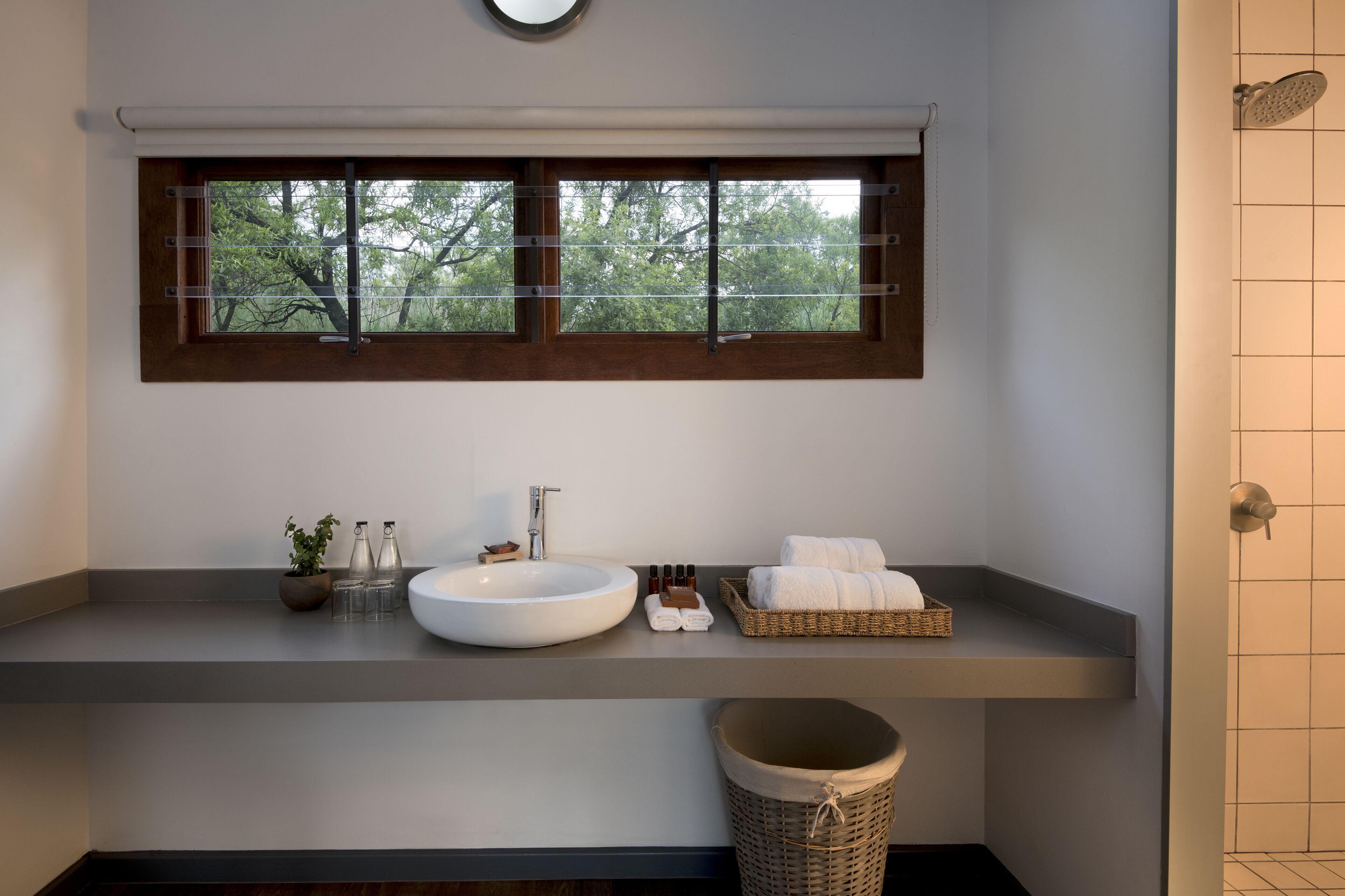 Une salle de bain dotée d’une grande fenêtre, d’un lavabo rond, d’un miroir et d’un espace douche.