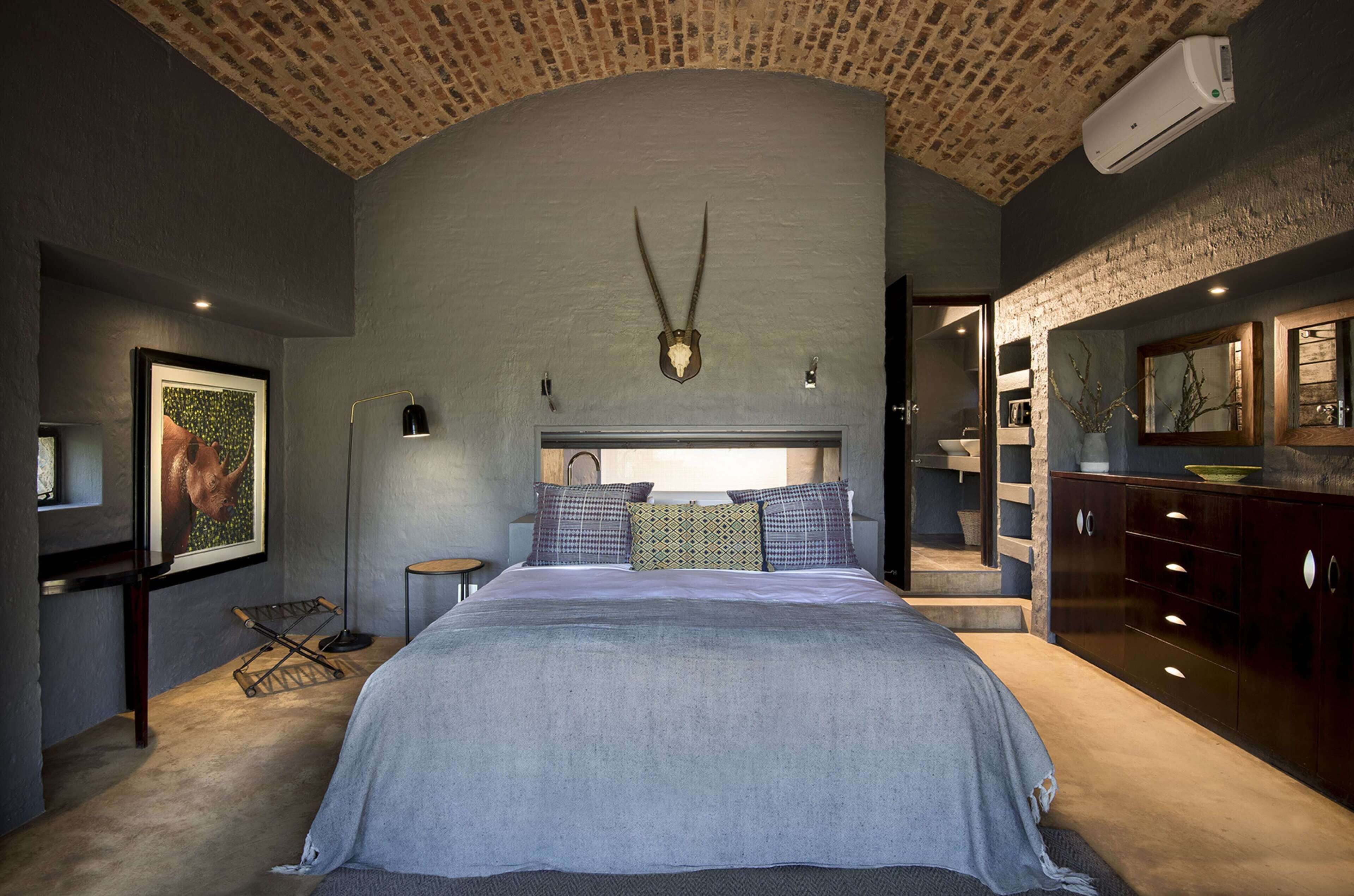 A bedroom with a large bed, a headboard with a skull decoration, a hanging light, and a large mirror.