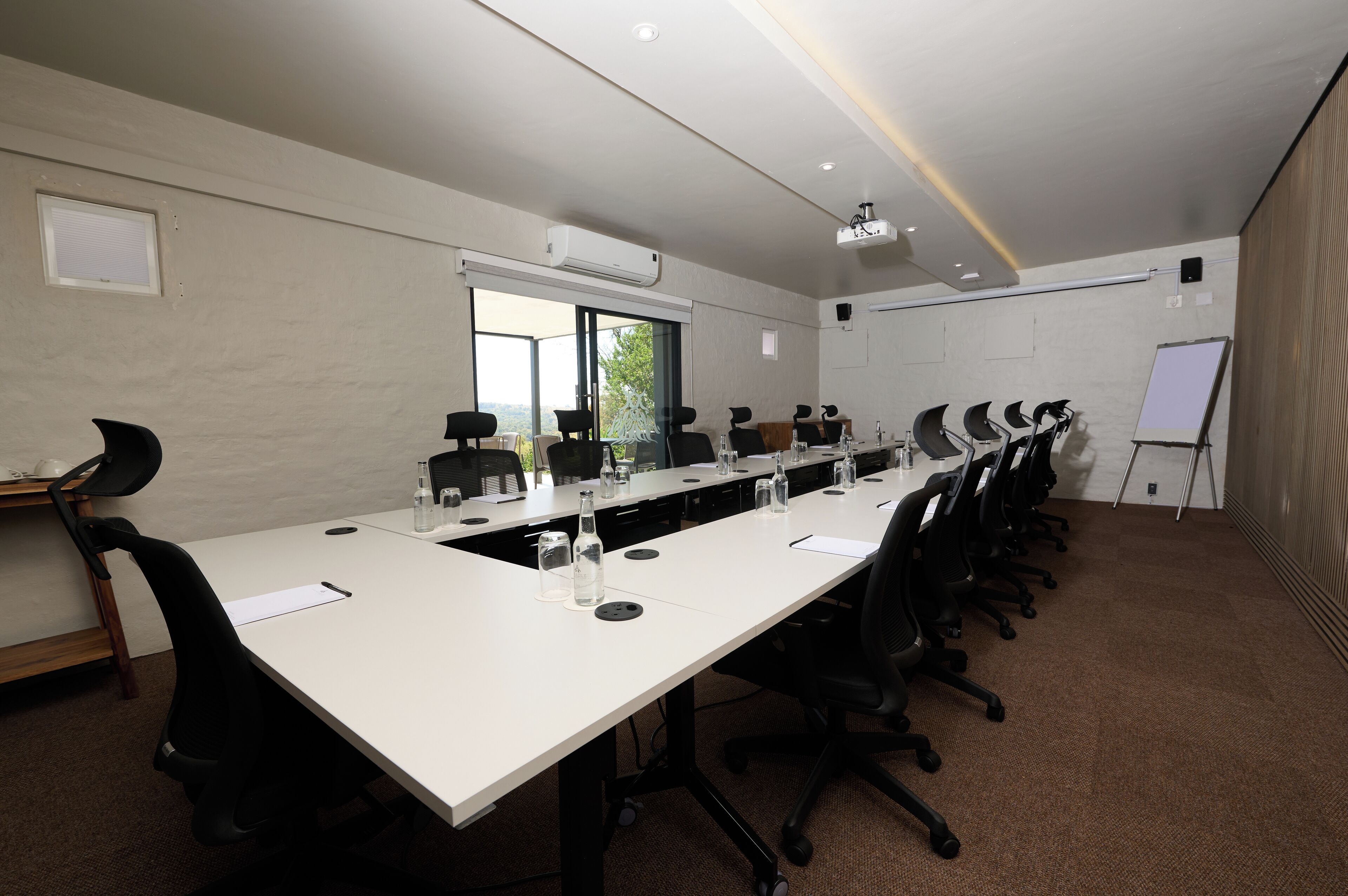 A conference room with a long table, black chairs, a whiteboard, and an air conditioning unit.