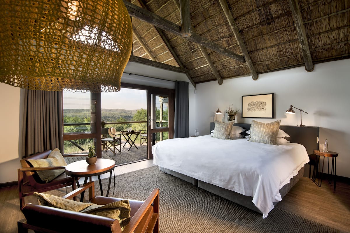 A spacious bedroom with a large bed, a balcony with a view, and a dining area with a table and chairs.