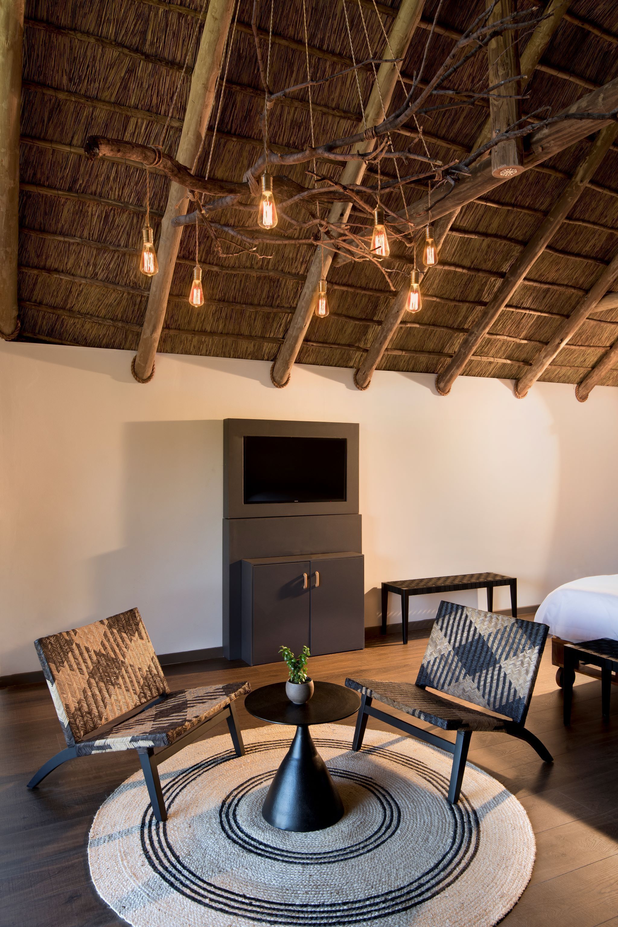 A room with a thatched ceiling, wooden beams, a round table with chairs, a flat-screen TV, and a small potted plant.