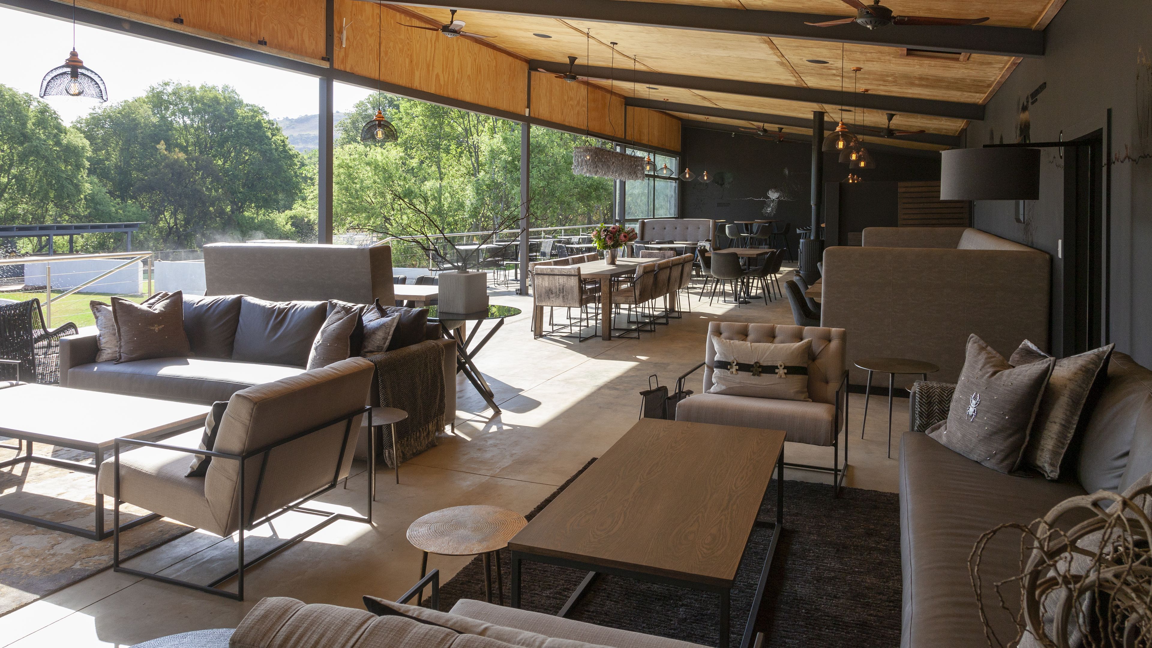 An open-plan lounge with sofas, tables, and chairs, large windows offering a view of greenery.