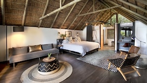 A bedroom with a bed, a sofa, a coffee table, and a chair. There is a ceiling with wooden beams and a thatched roof. - Cradle Boutique Hotel (Muldersdrift)
