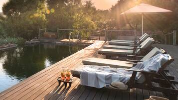 Relax on the deck overlooking the calm water, surrounded by lush greenery and shaded seating.