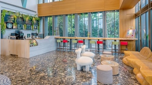Un hall d’entrée moderne doté d’un comptoir de réception, d’un espace salon et de grandes fenêtres offrant une vue sur les arbres.