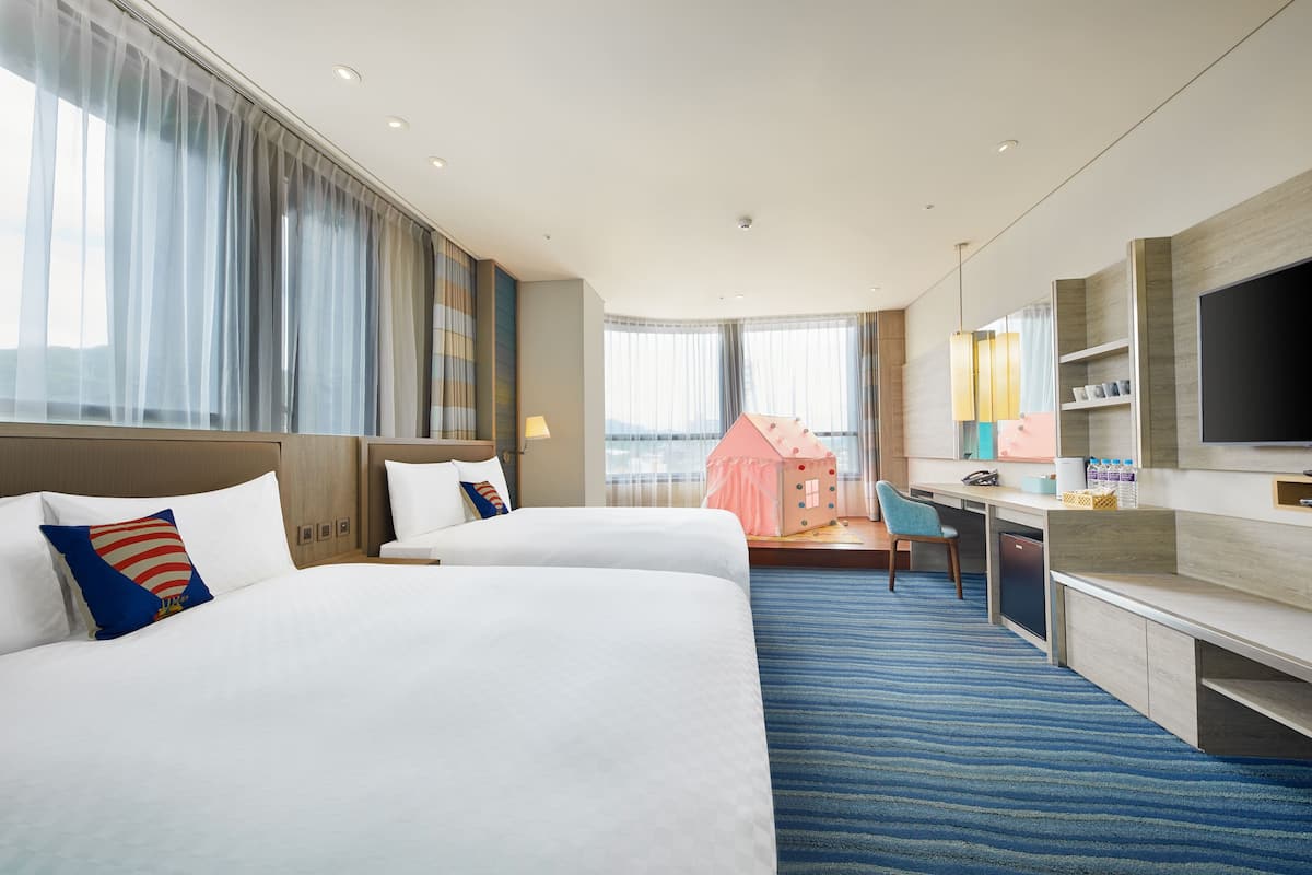Habitación de hotel con dos camas, un escritorio, un televisor y vistas a la ciudad.