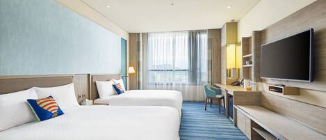 Habitación de hotel con dos camas, un escritorio, televisión y un ventanal con cortinas.
