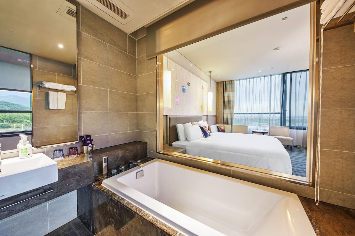 Un baño de hotel moderno con un espejo grande, una bañera, un lavabo y una ventana que ofrece vistas al exterior.