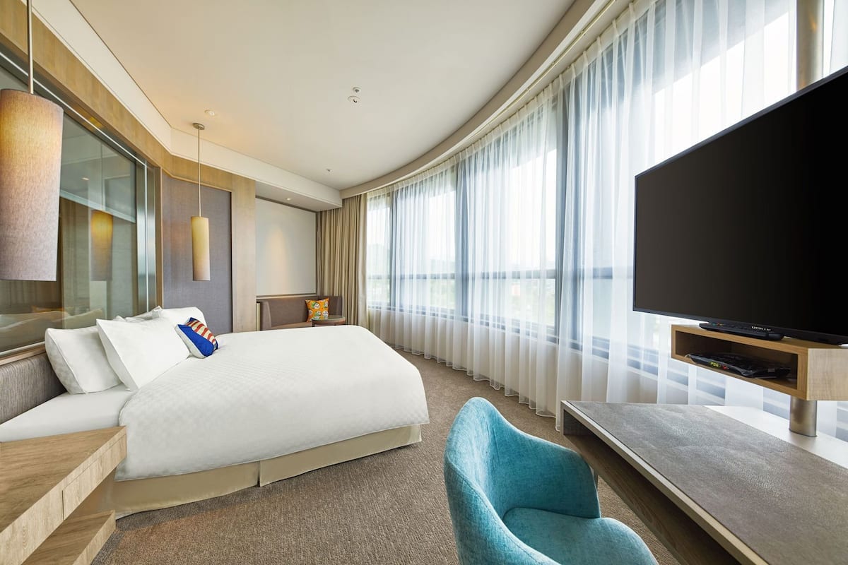 Habitación de hotel con una cama grande, televisión, una silla y vistas al exterior.