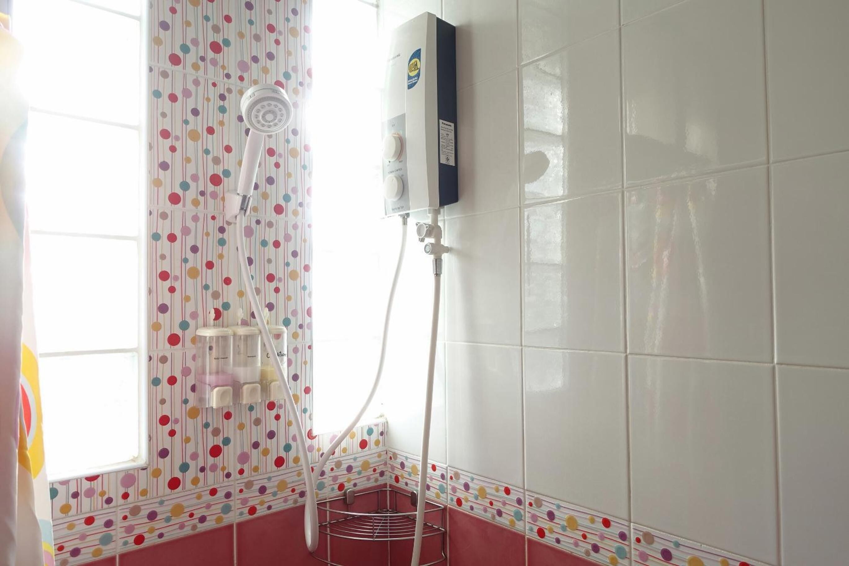 A bathroom with a shower, a white tiled wall, and a colorful polka dot curtain.