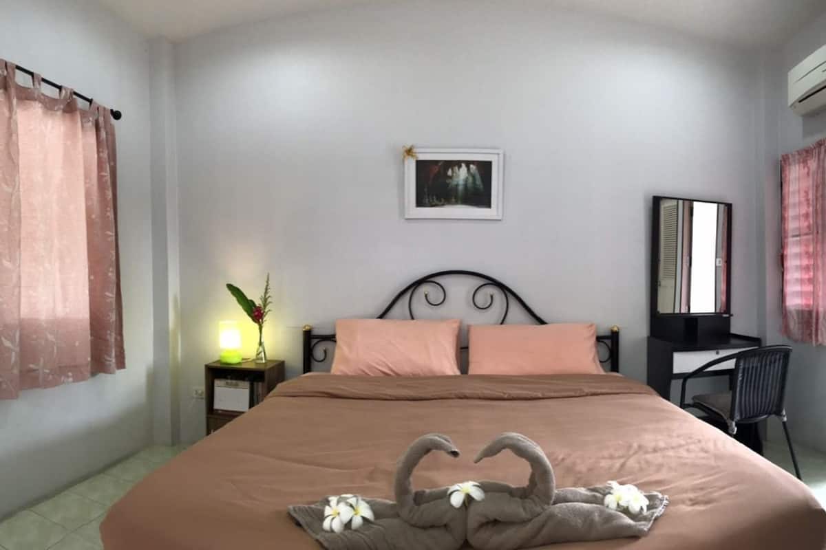 A bedroom with a bed, a nightstand, a chair, a desk, a mirror, and a door.