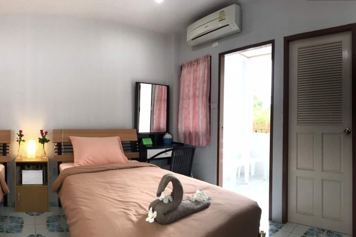 A hotel room with two beds, a desk, a chair, an air conditioner, and a door.