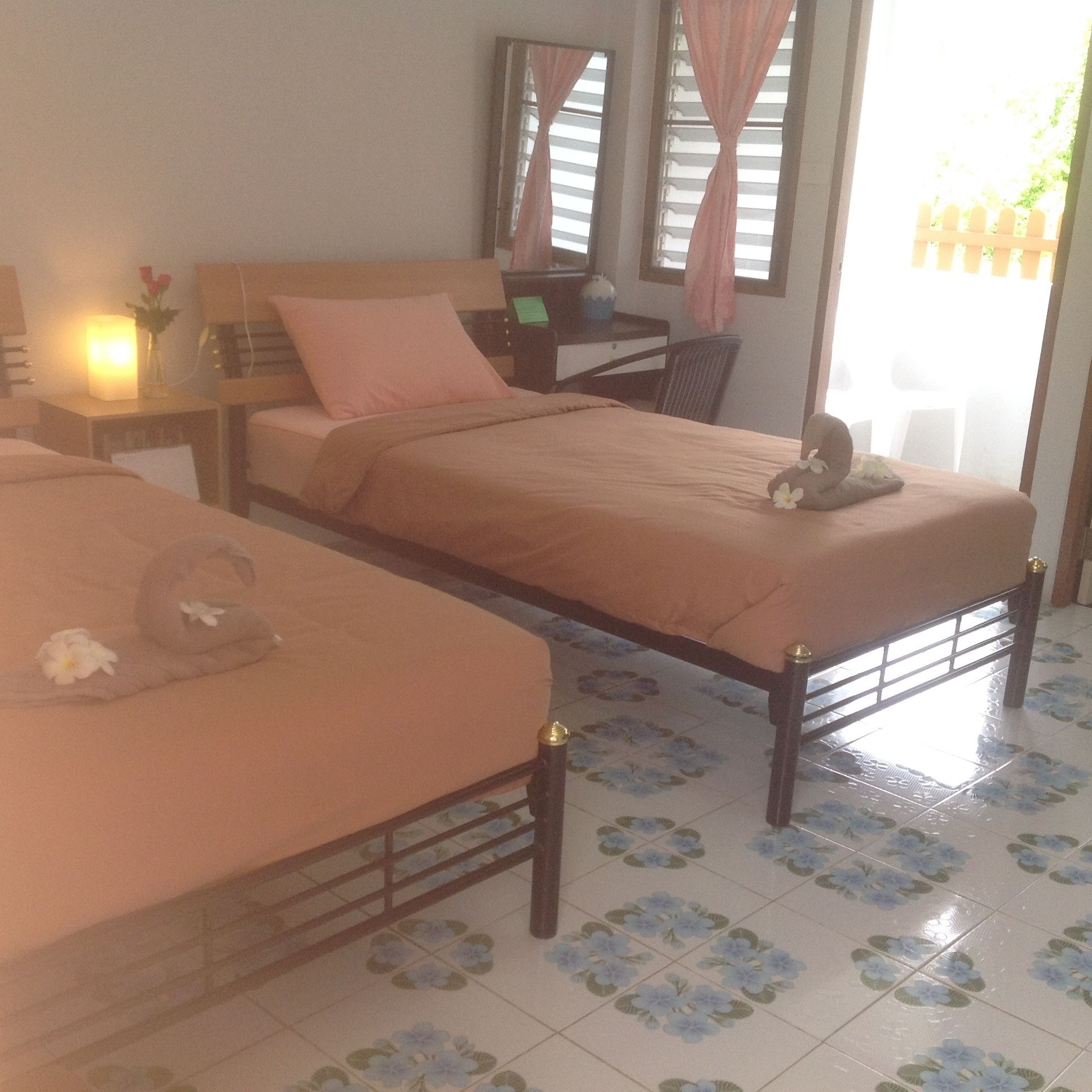Una habitación con dos camas individuales, un escritorio, una silla y una mesita de noche con una lámpara.