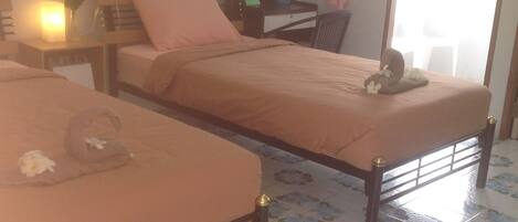 Una habitación con dos camas individuales, un escritorio, una silla y una mesita de noche con una lámpara.