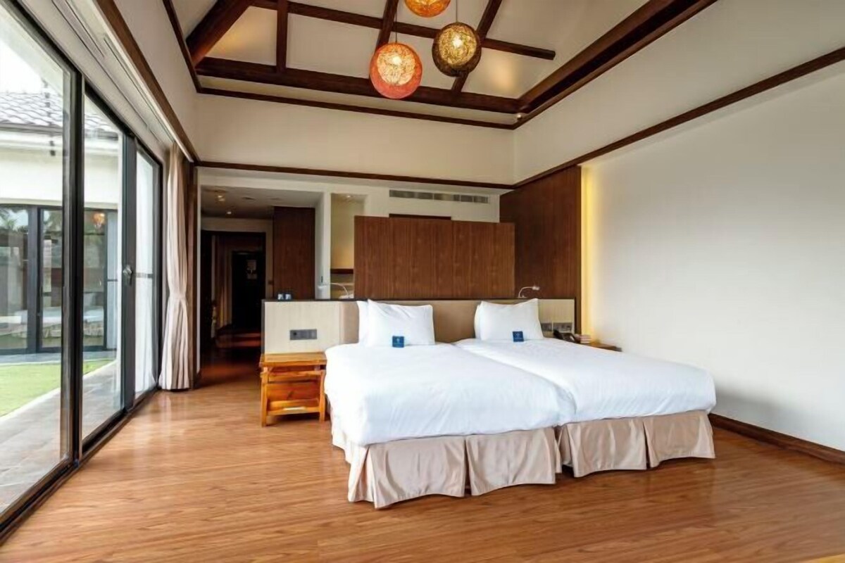 Une chambre d’hôtel moderne avec un grand lit, un plancher en bois et une vue dégagée sur l’extérieur grâce à de grandes fenêtres.