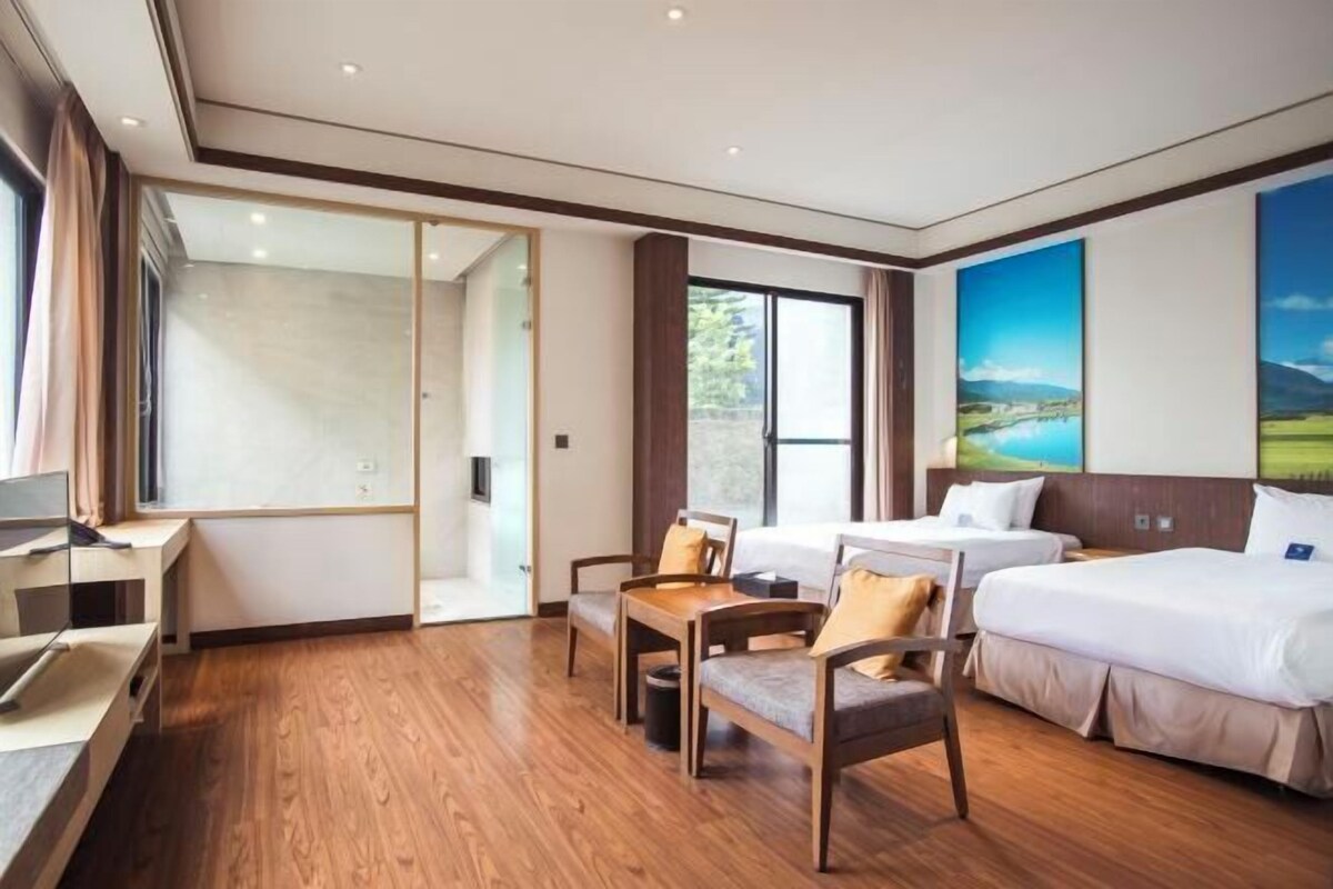 Une chambre d’hôtel avec deux lits, un bureau, une chaise et une grande fenêtre.