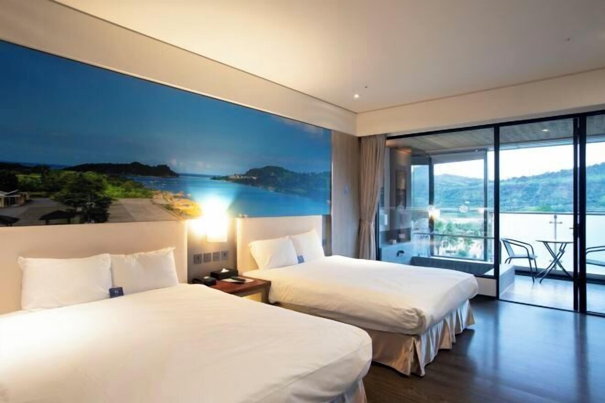 Une chambre d’hôtel avec deux lits, une grande fenêtre et un balcon donnant sur la mer.