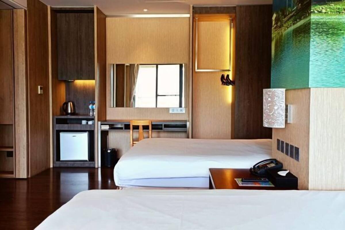 A hotel room with a bed, a desk, a chair, a small kitchenette, and a large window.