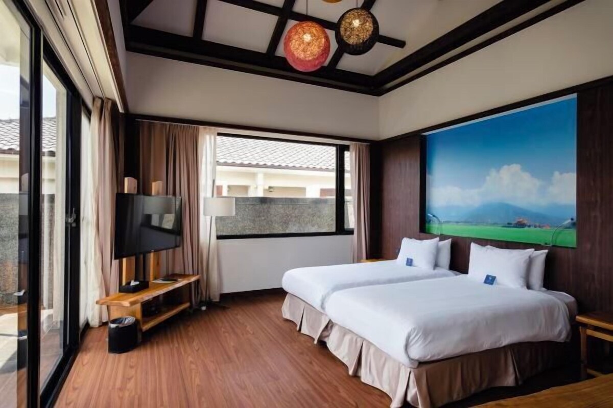 Une chambre d’hôtel avec un grand lit, une télévision, un tableau et une fenêtre donnant sur un beau paysage.