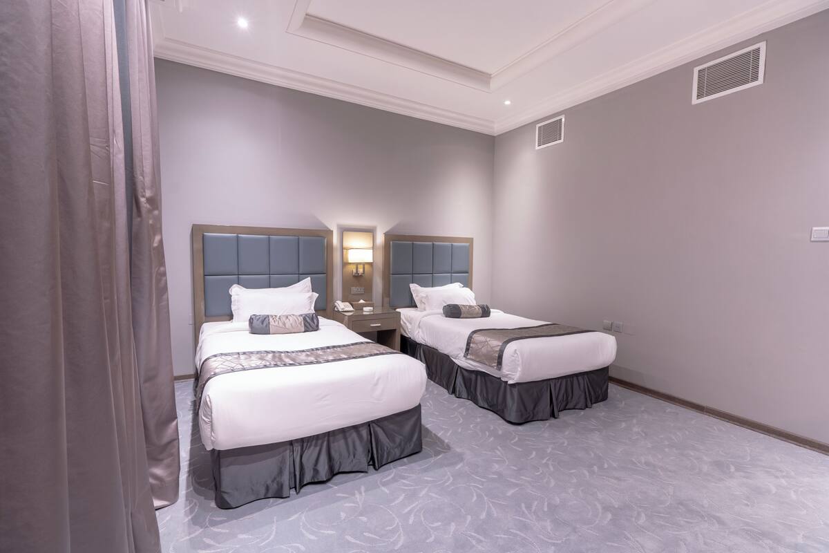 A hotel room with two beds, a nightstand, a lamp, and a mirror.