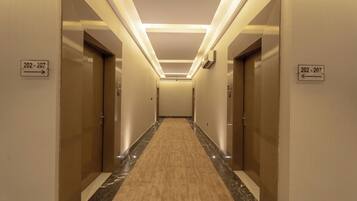 A hotel hallway with doors numbered 202-207, a carpeted floor, and a modern light fixture.