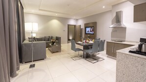 Ein modernes Wohnzimmer mit Sofa, Couchtisch und Fernseher. Es gibt einen Essbereich mit Tisch und Stühlen. Die Küche ist mit einem Herd und Schränken ausgestattet.