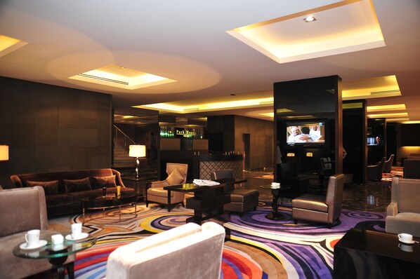 A modern hotel lobby with a seating area, a television, and a bar. - Park House Hotel Suite (Riyadh)