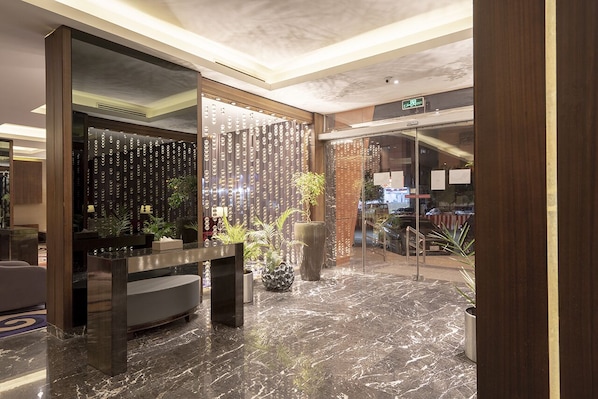 A modern lobby with a marble floor, a reception desk, and a decorative wall with vertical elements.